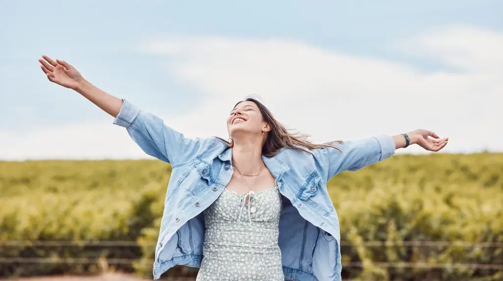 Happy, freedom and smile with woman in nature for peace, relax and youth with blue sky mockup. Journey, adventure and happiness with girl enjoying outdoors for summer break, vacation and holiday