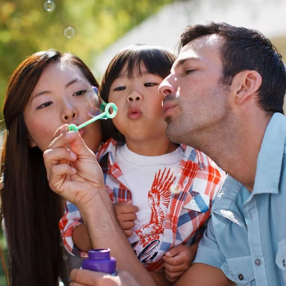 A mother, daughter, and father blowing bubbles together