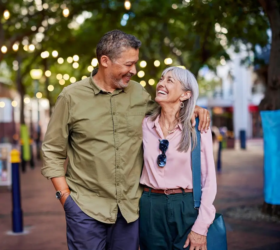 Couples Therapy. Happy multiethnic man and smiling woman enjoy a romantic evening outdoors. Mature couple shares a loving moment while walking in a european city. Smiling senior couple walks closely together under string lights with copy space.