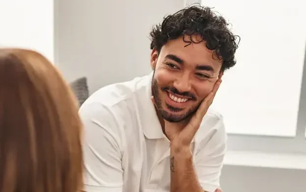DBT Therapy. A man with dark curly hair smiling and attending a therapy session.