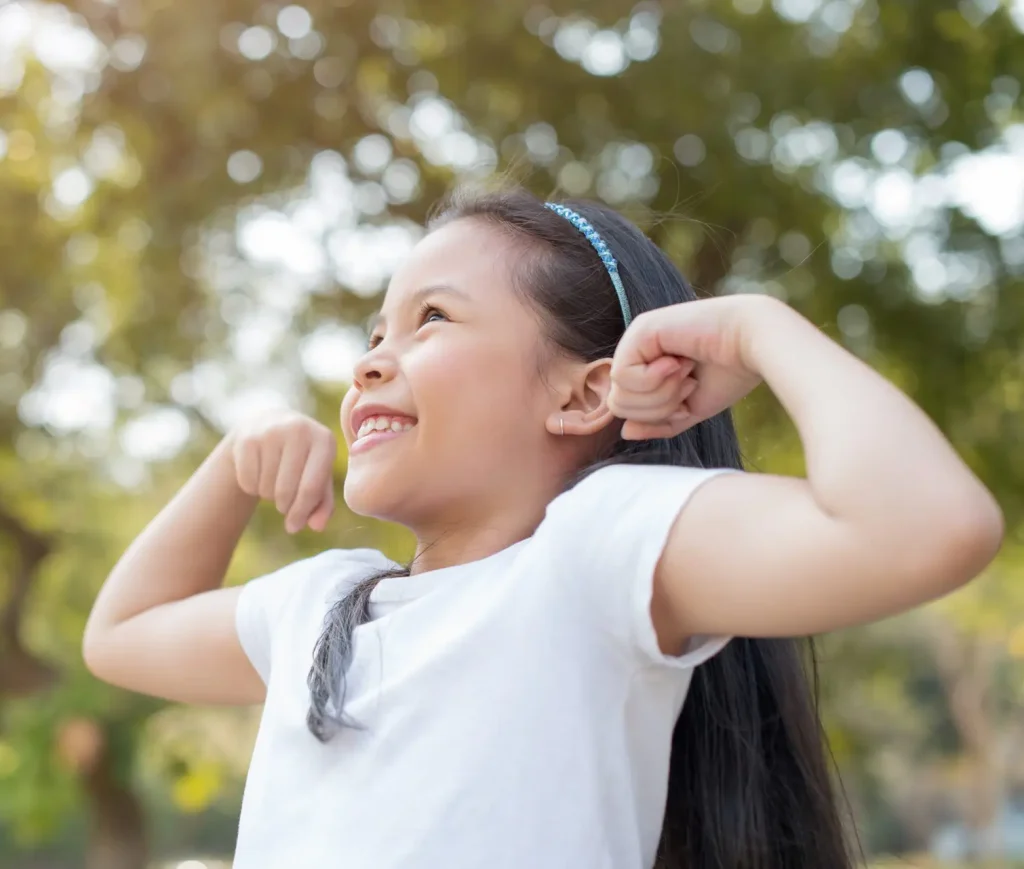 Happy little girl standing with big smile and showing arms muscles smiling proud.