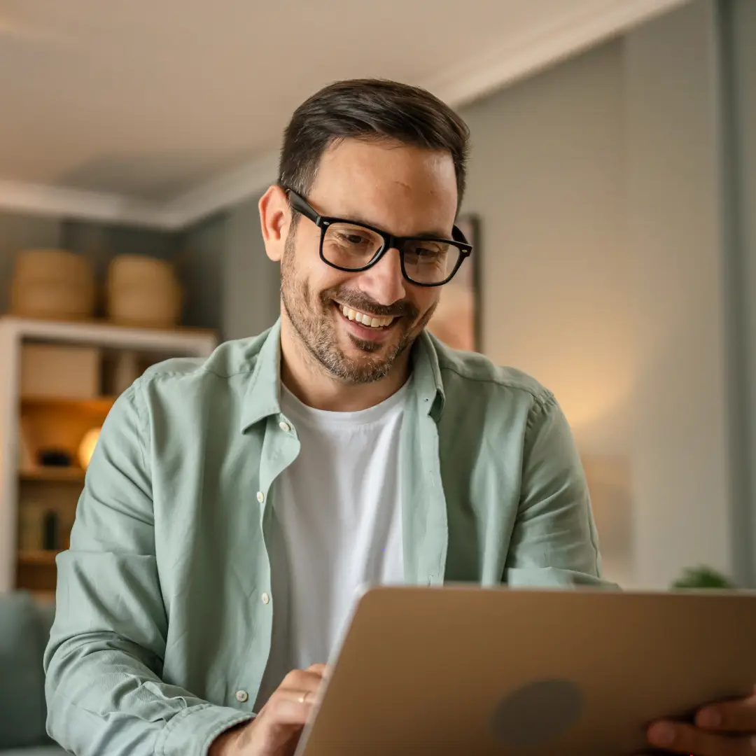 EMDR Therapy. Man wearing a seafoam coloured shirt and glasses smiling and looking at his laptop