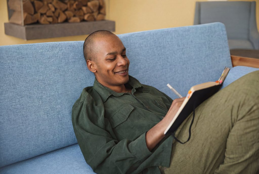 Person writing in a journal while relaxing on a sofa at home